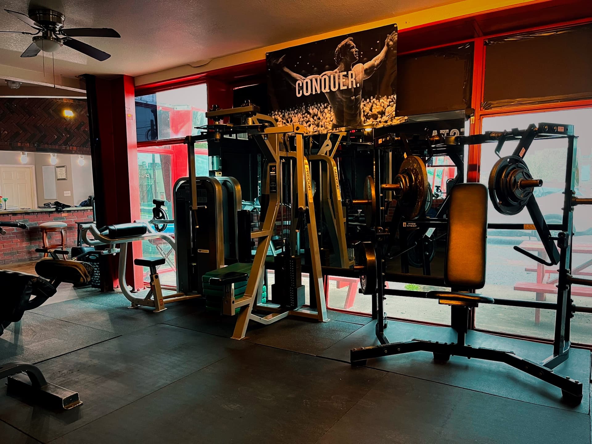 The Alpha Fitness weight floor at night, benches and racks under deep red light below a Conquer banner