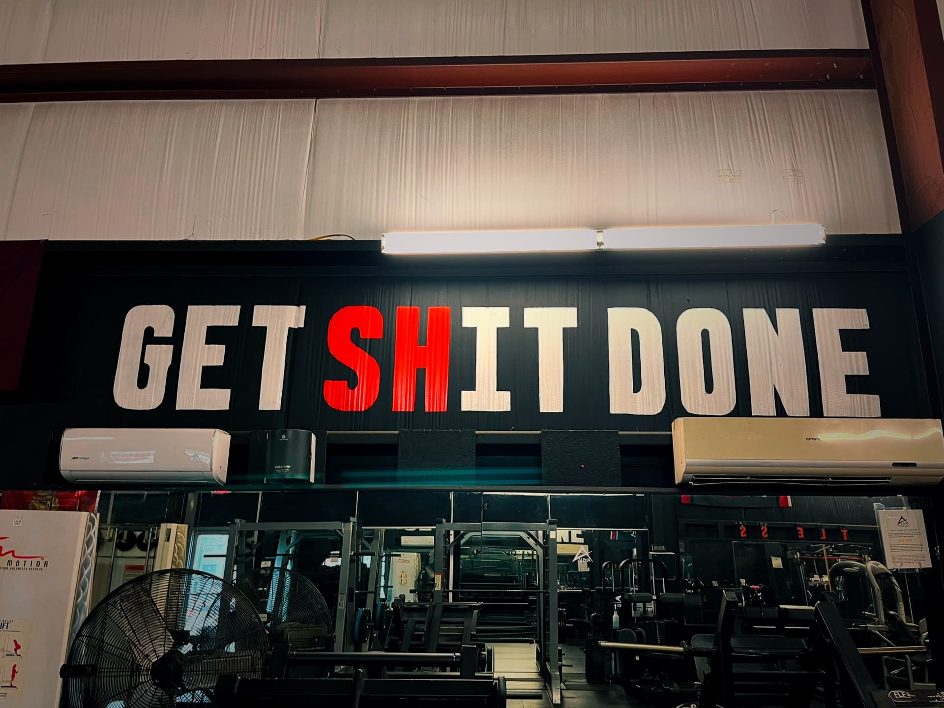 The words Get Shit Done painted in large letters across the black gym wall, the SH in red