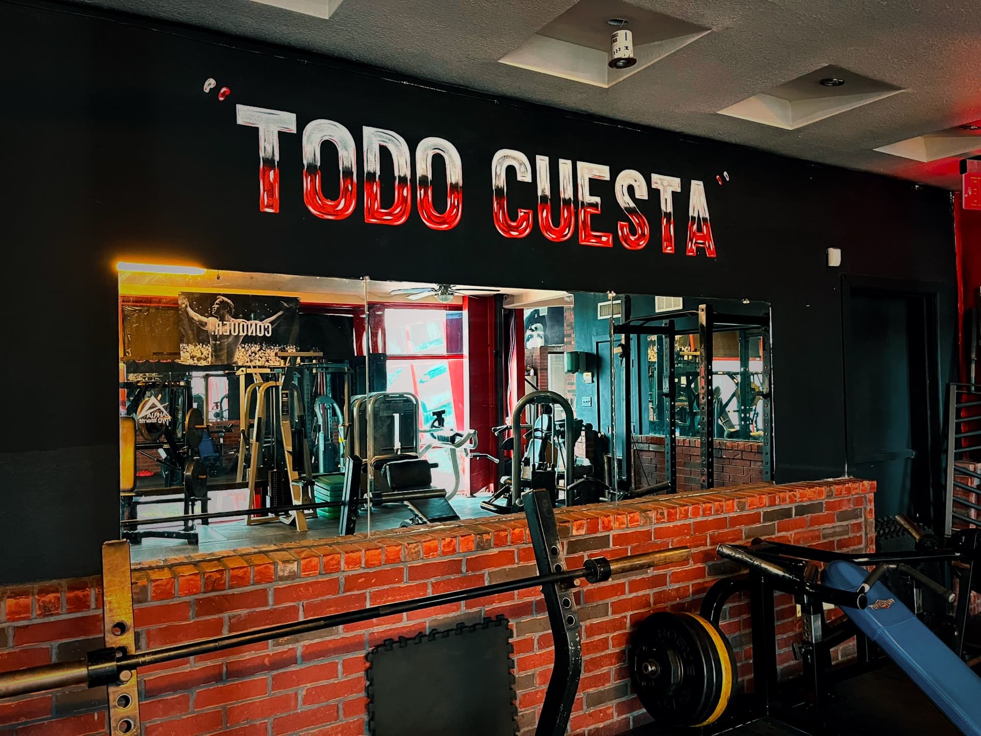 Todo Cuesta painted above the mirrors over a brick wall and a row of loaded barbells